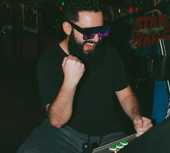 Man enjoying retro arcade gaming with colorful sunglasses and classic arcade setup.