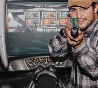 Young man aiming laser gun at arcade game with bright screens.